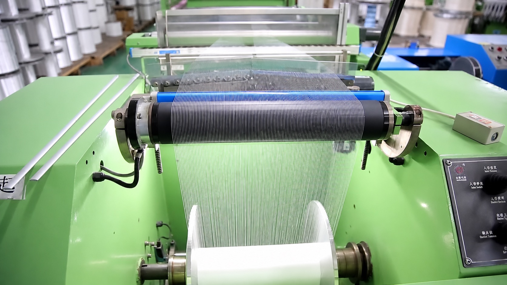 Narrow loom warp beam close-up  warp threads on blue tensioning roller, green ribbon weaving machine